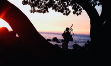 Silhouette Musician Playing Bagpiper Amidst Trees On Shore Against Sky During Sunset