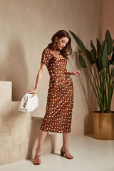 Wall Mural - Fashion model brunette hair wear brown dots silk dress sandals high heels accessory bag clothes date party walk interior journey summer collection plant flowerpot wall stairs beautiful woman tan skin