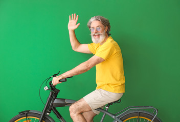 Wall Mural - Happy elderly man with bicycle on color background