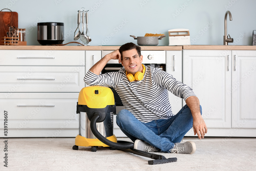 Young man with vacuum cleaner in kitchen