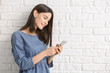 © Pixel-Shot - Beautiful young woman with mobile phone on white brick background