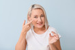 © Pixel-Shot - Mature woman putting in contact lenses against light background