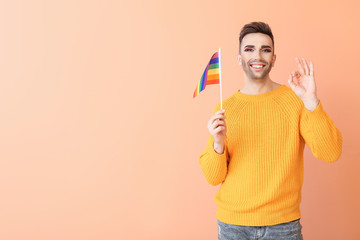 Wall Mural - Portrait of young transgender woman with flag of LGBT showing OK gesture on color background