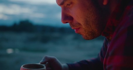 Wall Mural - a man is drinking hot tea in nature, campfire, camping, night, close up.