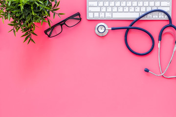 Doctor workplace. Stethoscope and computer keyboard on pink office desk top view copy space