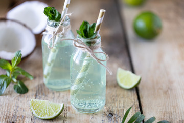 Two bottles of coconut water with mint and lime on a wooden table. Vegetarian drink. Mojito. Copy space