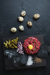 Wall Mural - Tartar made of raw marbled beef meat with other components, flatlay on a black stone background, vertical shot