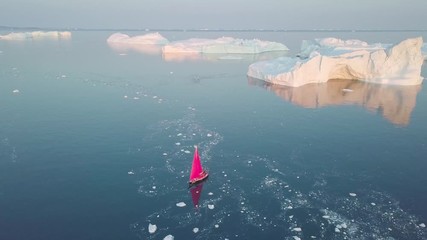 Wall Mural - Little red sailboat cruising among floating icebergs in Disko Bay glacier during midnight sun season of polar summer. Ilulissat, Greenland. Studying of a phenomenon of global warming. Unesco world