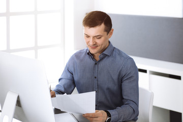 Businessman working with computer in modern sunny office. Headshot of male entrepreneur or company director at workplace. Business concept