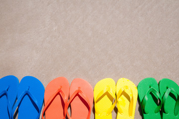Wall Mural - Group of flip-flops in bright summer colors lined up on smooth sand beach