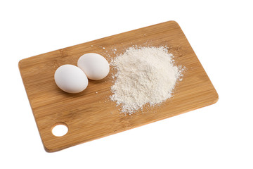 two white eggs on a wooden board and next to a handful of flour