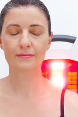 Smiling woman with fibromyalgia in front of infrared light lamp, thermotherapy treatment.