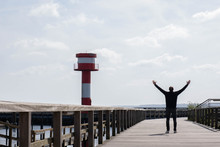 A Man On A Bridge Near The Lighthouse And The Sea Raised His Hands Up