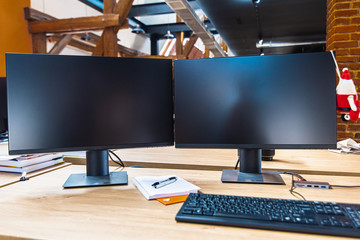 Desktop view, two computer screens, keyboard, mouse and computer have a blank black screen on a wooden desk and an office background