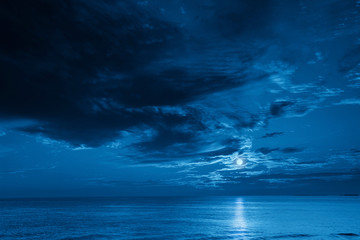Wall Mural - this photo illustration of a deep blue moonlit ocean and sky at night would make a great travel back