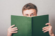 The man in glasses covered his face with a book. On a gray background.