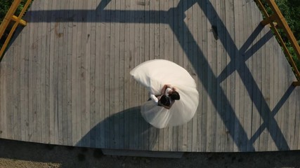 Wall Mural - Groom holds the bride in his arms and whirls in a wedding dance on a viewing platform in the mountains. Aerial view 2020