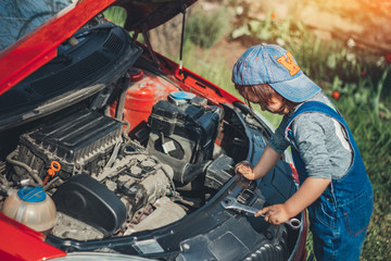 Little child trying to fix broken real car. Dreaming to be auto technician