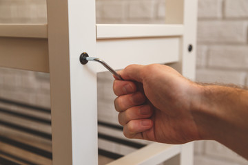 Assembling of furniture, closeup hex wrench in hand, furniture screw screwed into board of bench