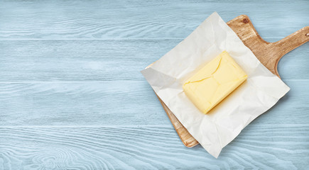 Piece of butter on package paper and wooden board. Top view of butter on blue wooden background.