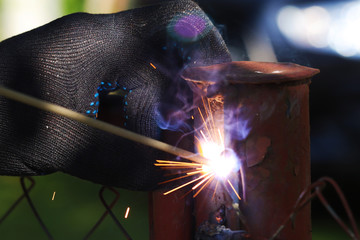 Red hot sparks from metal welding closeup. Gloved hand in the background