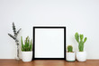 © Jenifoto - Mock up black square frame with potted plants and branch decor. Wooden shelf against a white wall. Copy space.