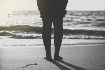 Barefoot woman standing on the beach during sunset time,Back and white toned