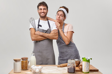 Wall Mural - Happy satisfied couple finish cooking, tired wife with dirty face leans at husbands shoulder, prepare tasty meal for family, plan menu together, pose indoor. Culinary, cuisine and baking concept