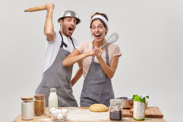 Wall Mural - Joyful family couple have fight with cooking utensils, have fun during culinary process at kitchen, spend time together indoor. Happy partners use kitchenware for fencing, cook breakfast at home