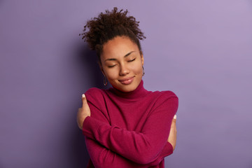 Canvas Print - I love myself. Tender romantic woman embraces own body, hugs herself, closes eyes from pleasure, wears soft turtleneck just for cold weather, feels comfort, stands indoor against purple wall