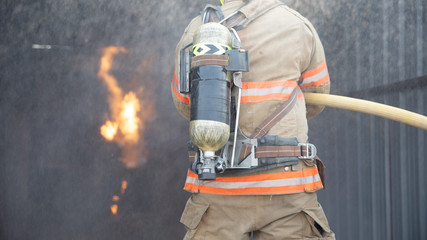 Wall Mural - Rear view of Fireman wear fire protection suit walking into the fire training room and Spray water Fire at fire station. Training fire drill Concept.