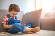 © Dragana Gordic - Cute young little boy holding smart phone. He is sitting a sofa and is focused on mobile phone. Growing up in a technology-based world.