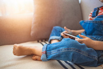 Cute boy using a mobile phone. A little boy looking to smartphone lying on the couch at home. Toddler boy using tablet or smartphone. Cute three years old boy sitting at home using digital device.