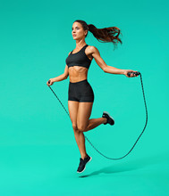 Sporty Girl Exercising With Skipping Rope. Photo Of Girl In Black Sportswear On Turquoise Background. Dynamic Movement. Full Length. Sports And Healthy Lifestyle