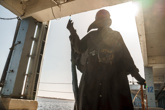 plague doctor in empty city on empty pier holds vaccine