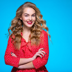 Wall Mural - Portrait of a happy young blonde. Beautiful smiling girl with long white hair. Model in a red shirt poses in studio. People with crossed arms.  Caucasian woman with a good smile. Happiness concept.