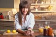 © a.dl - Happy white woman holding phone at home, making breakfast, drinking coffee in the kitchen in the morning.