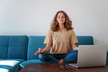 Calm healthy young woman taking break  with eyes closed sit on blue sofa with laptop,  breathing exercise at home feel stress, mind concept