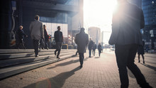Office Managers And Business People Commute To Work In The Morning Or From Office On A Sunny Day On Foot. Pedestrians Are Dressed Smartly. Successful People Walking In Downtown. Cloudy Day In Downtown