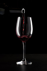 Red wine being poured into a glass and splashing over the side. Low key black background.