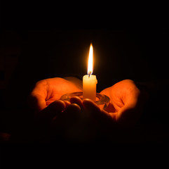 Hands holding a burning candle in dark room