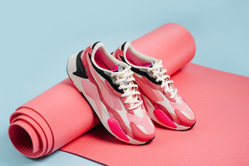 Pair of   women's sneakers with pink yoga mat on blue background. Fashion blog or magazine concept. Healthy lifestyle.  Home  workout.