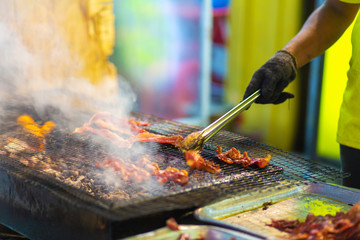 Food seller at night street market in Asia, grilling pieces of meat on the grill.