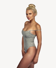 Young blonde woman wearing casual grey bodysuit on white background. Portrait of slim sexy girl with perfect face and skin in cotton undrewear. Mockup.