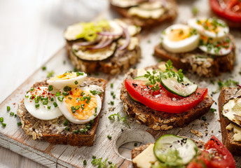 Wall Mural - A set of breakfast sandwiches made from homemade buckwheat bread with various toppings on a wooden rustic board, close up