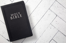A Black Holy BIble On A White Wooden Table