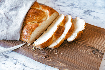 Homemade Jewish traditional challah bread on rustic wooden cutting board with knife. Top view of warm fresh baked challah cut in slices