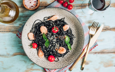 Wall Mural - Black pasta with seafood. Traditional Italian cuisine - pasta with shrimp, tomato and basil in a ceramic plate on a rustic background. Flat lay, top view.