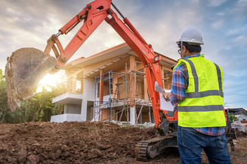 Wall Mural - Construction engineer Stands in control of work in the construction site, house or building by excavators machine and House in construction site on background.