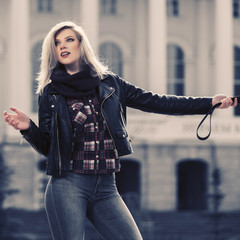 Wall Mural - Young fashion blonde woman with handbag in leather jacket walking on city street